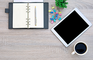 A desk with a planner, paper clips, coffee, and a tablet computer