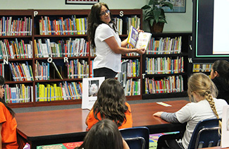 Estella reading Lunch Lady book to students in the library
