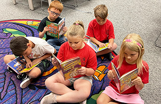 Group of five elementary students sitting in classroom reading books 